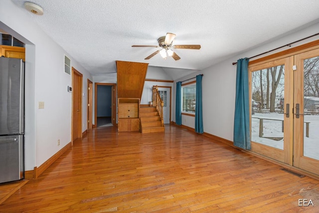 unfurnished living room with ceiling fan, a textured ceiling, french doors, and light wood-type flooring