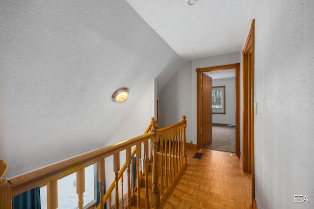 hallway with light parquet flooring, vaulted ceiling, and a textured ceiling