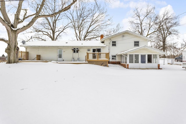 snow covered rear of property featuring a sunroom and a wooden deck