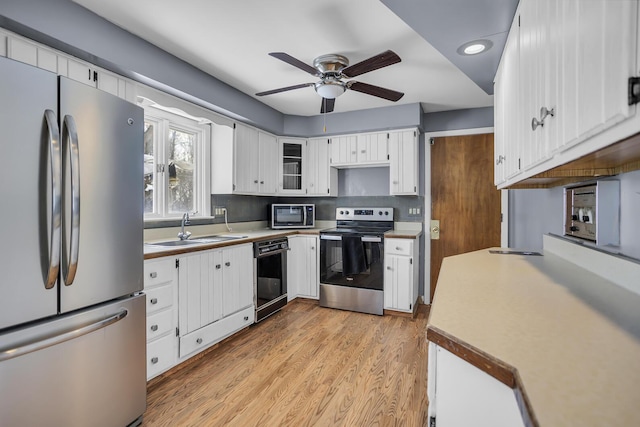 kitchen featuring stainless steel appliances, light hardwood / wood-style floors, white cabinets, ceiling fan, and sink