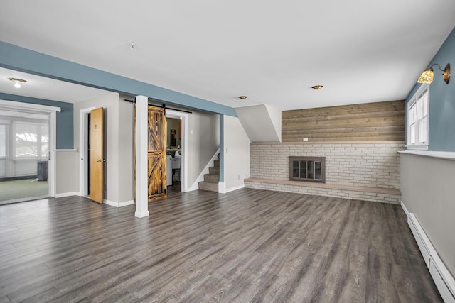 unfurnished living room with dark hardwood / wood-style flooring, a baseboard heating unit, a barn door, and a fireplace