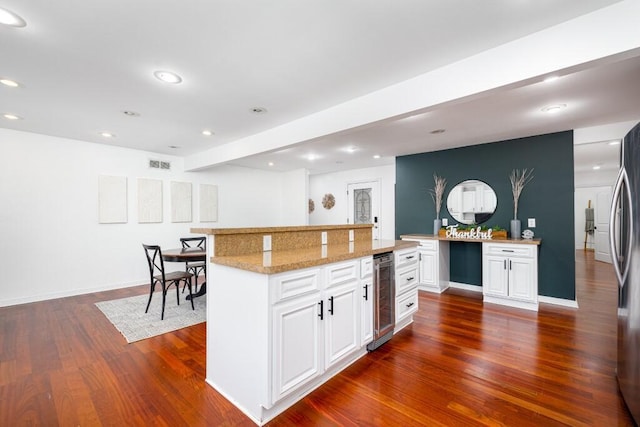 kitchen featuring a kitchen island, white cabinets, wine cooler, dark hardwood / wood-style flooring, and light stone countertops