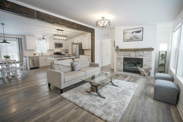 living room with sink, dark hardwood / wood-style flooring, lofted ceiling with beams, and a stone fireplace