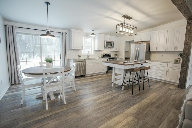 kitchen with appliances with stainless steel finishes, pendant lighting, white cabinets, and vaulted ceiling