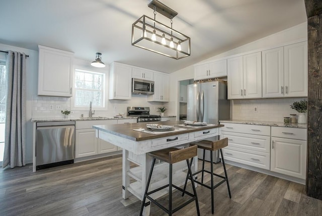 kitchen with vaulted ceiling, hanging light fixtures, white cabinets, appliances with stainless steel finishes, and sink