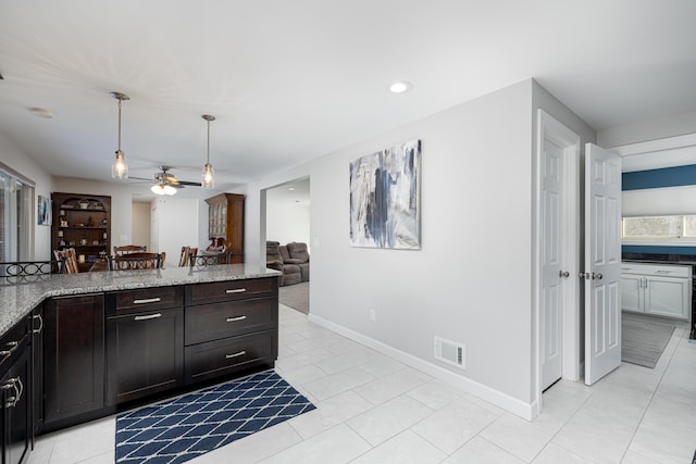 kitchen featuring pendant lighting, light tile patterned floors, ceiling fan, dark brown cabinets, and light stone counters