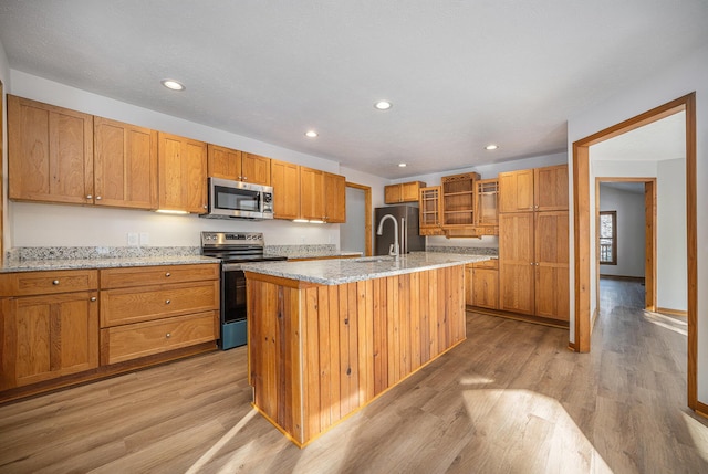 kitchen featuring sink, appliances with stainless steel finishes, light stone countertops, an island with sink, and light wood-type flooring