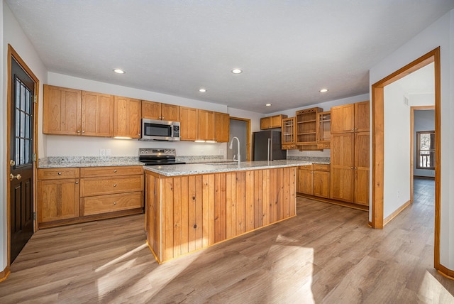 kitchen featuring sink, a kitchen island with sink, light stone counters, stainless steel appliances, and light wood-type flooring