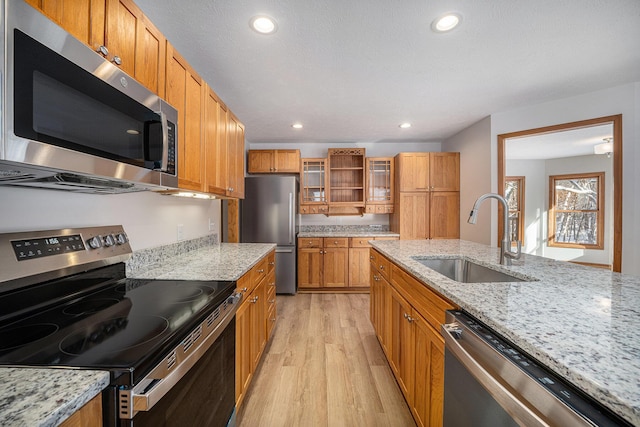 kitchen featuring stainless steel appliances, sink, light stone counters, and light hardwood / wood-style floors