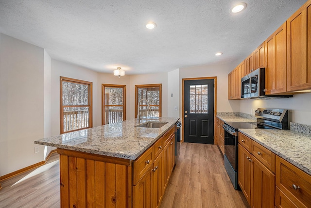 kitchen with appliances with stainless steel finishes, an island with sink, sink, a textured ceiling, and light hardwood / wood-style flooring