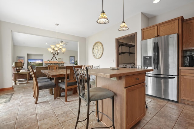 kitchen with hanging light fixtures, stainless steel fridge, a kitchen island, ceiling fan, and a kitchen breakfast bar