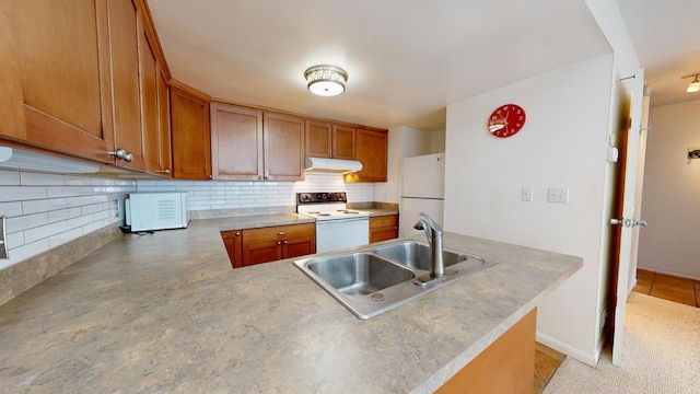 kitchen featuring white appliances, kitchen peninsula, decorative backsplash, and sink