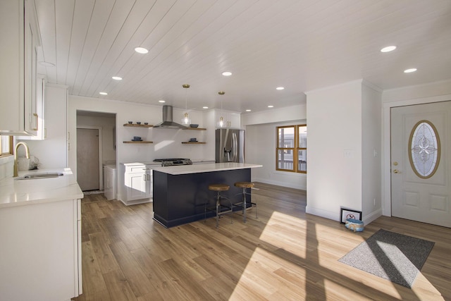 kitchen with stainless steel fridge, wall chimney range hood, a kitchen island, white cabinets, and sink