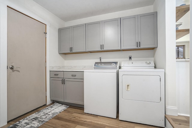 clothes washing area with washer and clothes dryer, light hardwood / wood-style flooring, and cabinets