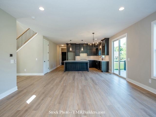 kitchen with backsplash, light wood-type flooring, a kitchen island, pendant lighting, and sink