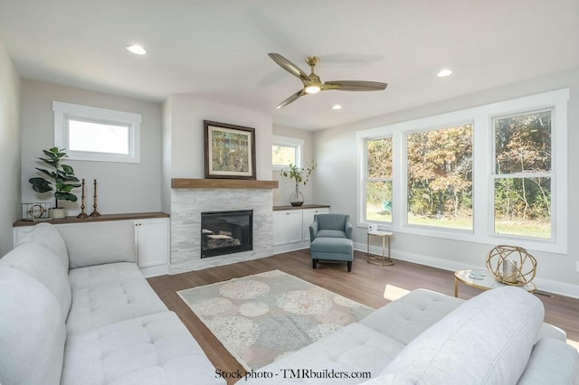 living room with ceiling fan, wood-type flooring, a tile fireplace, and a healthy amount of sunlight