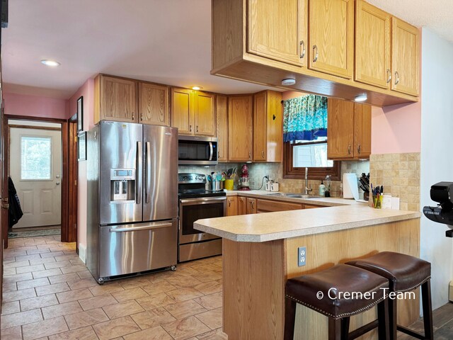 kitchen with kitchen peninsula, sink, tasteful backsplash, a kitchen bar, and stainless steel appliances