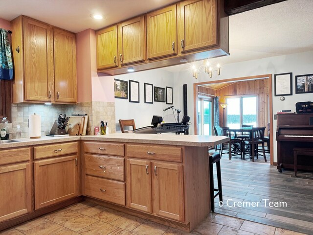 kitchen with kitchen peninsula, sink, light wood-type flooring, tasteful backsplash, and a kitchen bar