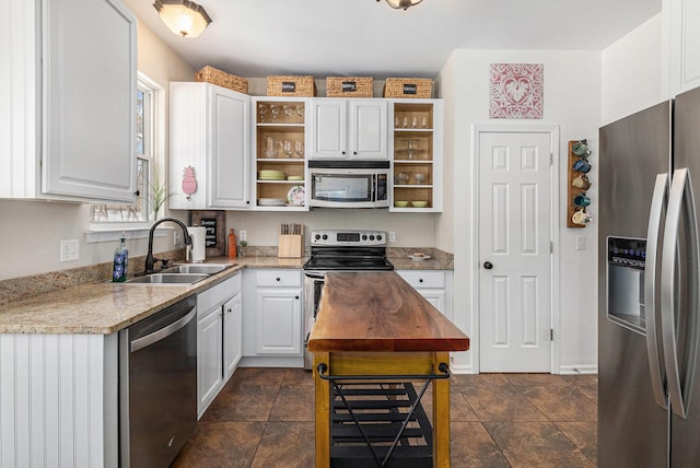 kitchen with appliances with stainless steel finishes, a healthy amount of sunlight, white cabinets, light stone counters, and sink