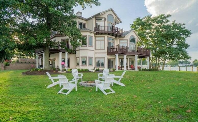 rear view of house with a yard, a balcony, and a fire pit