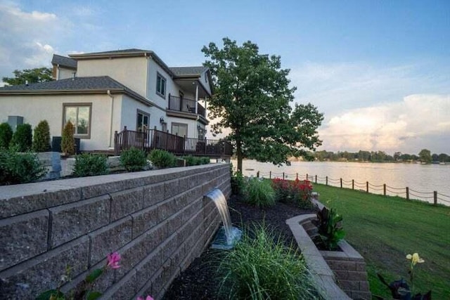 property exterior at dusk with a lawn, a water view, and a balcony