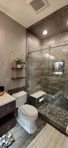 bathroom featuring toilet, vanity, and tiled shower