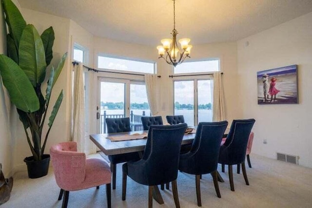 dining room featuring a water view, light colored carpet, and a chandelier