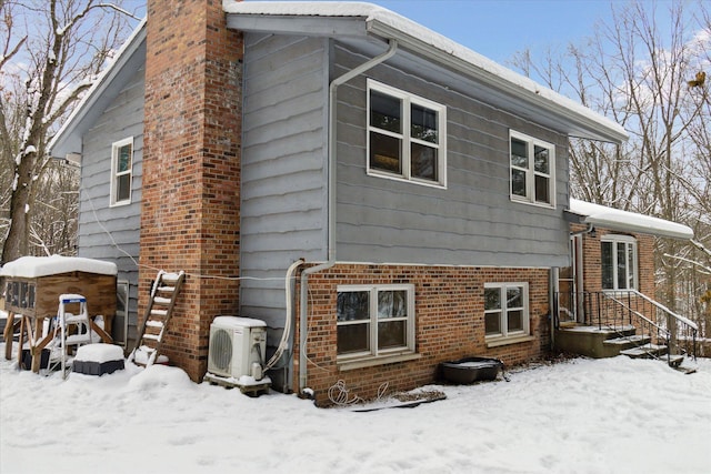 snow covered rear of property featuring ac unit