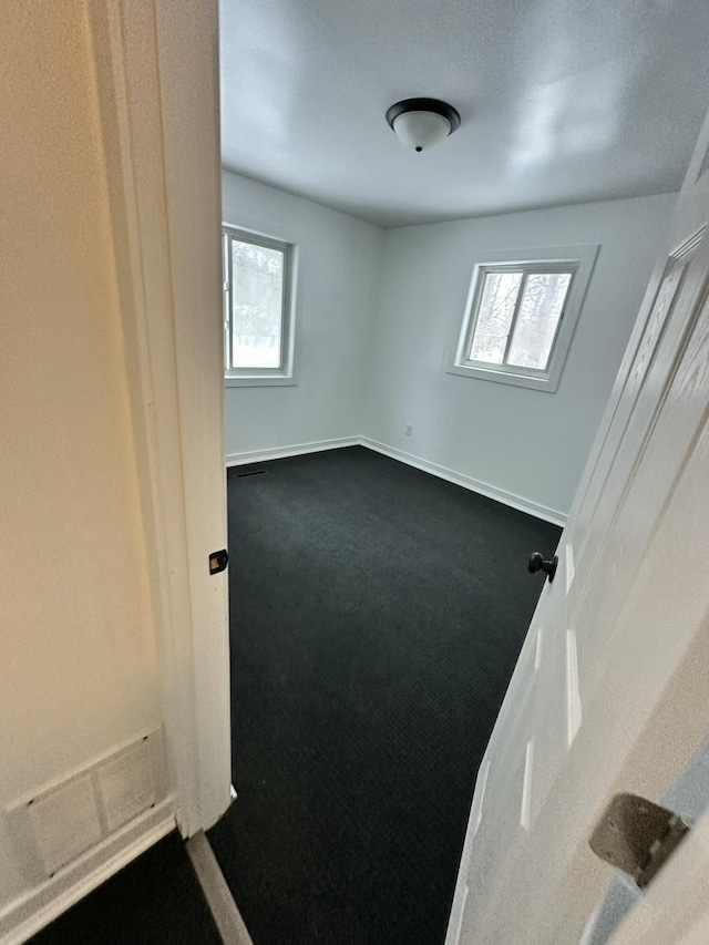 empty room featuring plenty of natural light and dark carpet