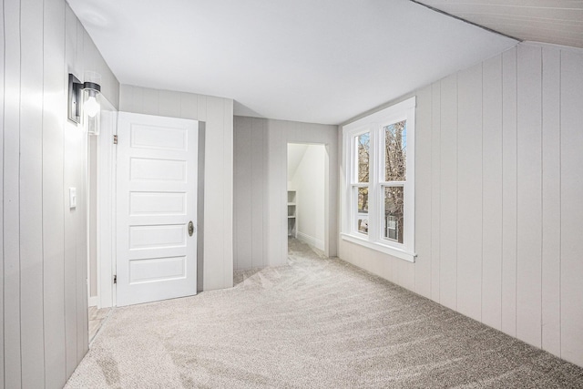 corridor with light colored carpet, vaulted ceiling, and wood walls