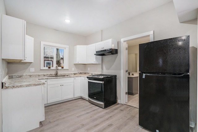 kitchen with white cabinets, gas stove, sink, black fridge, and light hardwood / wood-style flooring