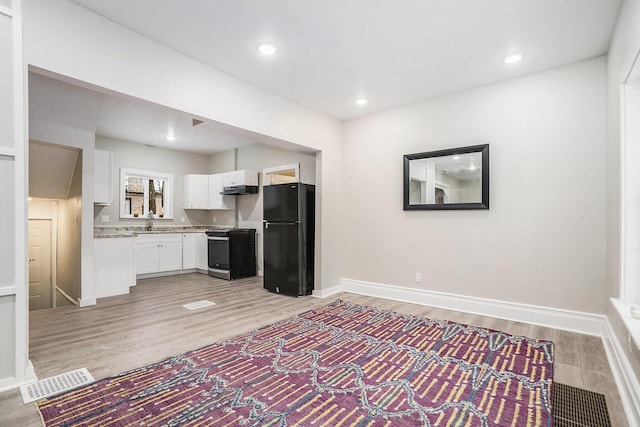 kitchen featuring black fridge, white cabinetry, light wood-type flooring, light stone countertops, and stainless steel range oven