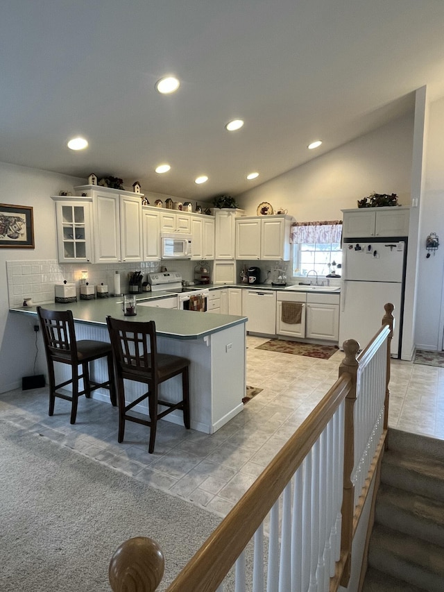 kitchen with vaulted ceiling, kitchen peninsula, a kitchen bar, white appliances, and white cabinetry