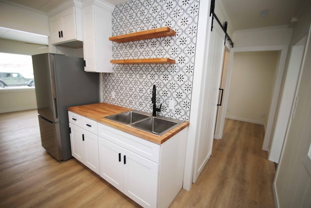 kitchen with white cabinetry, a barn door, butcher block countertops, crown molding, and sink