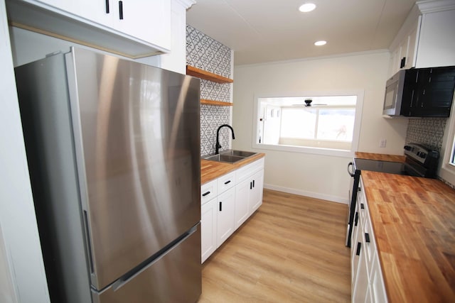 kitchen with stainless steel appliances, white cabinetry, wooden counters, and sink