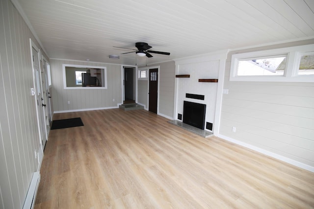 unfurnished living room with ceiling fan, light wood-type flooring, and wooden walls