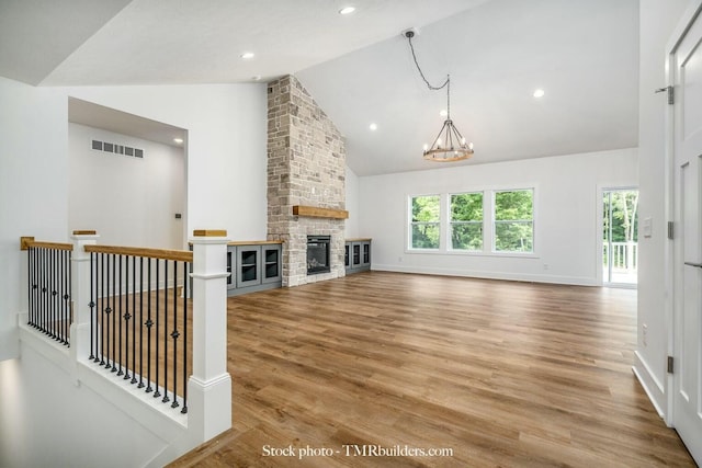 unfurnished living room featuring high vaulted ceiling, an inviting chandelier, a stone fireplace, and hardwood / wood-style flooring