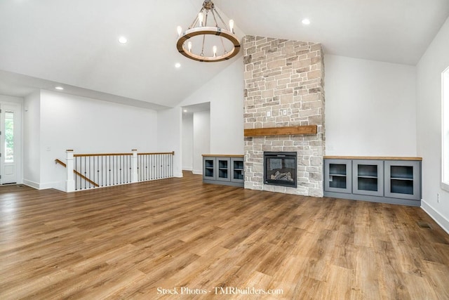 unfurnished living room featuring an inviting chandelier, hardwood / wood-style flooring, a stone fireplace, and high vaulted ceiling