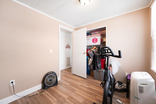 workout area with ornamental molding and light hardwood / wood-style floors