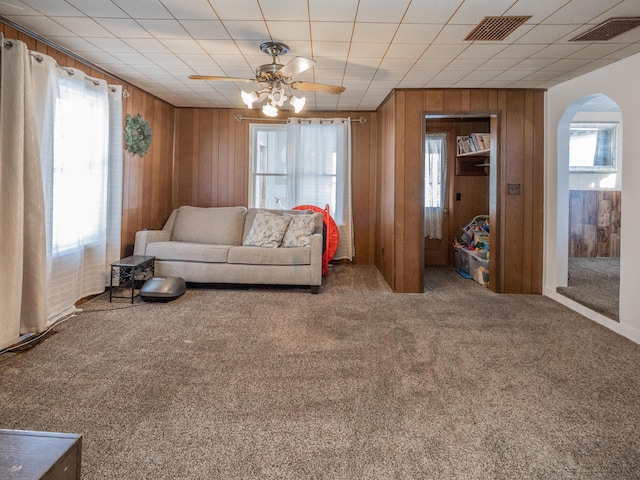 living room with ceiling fan, carpet flooring, and wooden walls