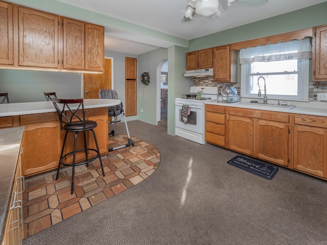 kitchen with a kitchen bar, decorative backsplash, white gas range, and sink