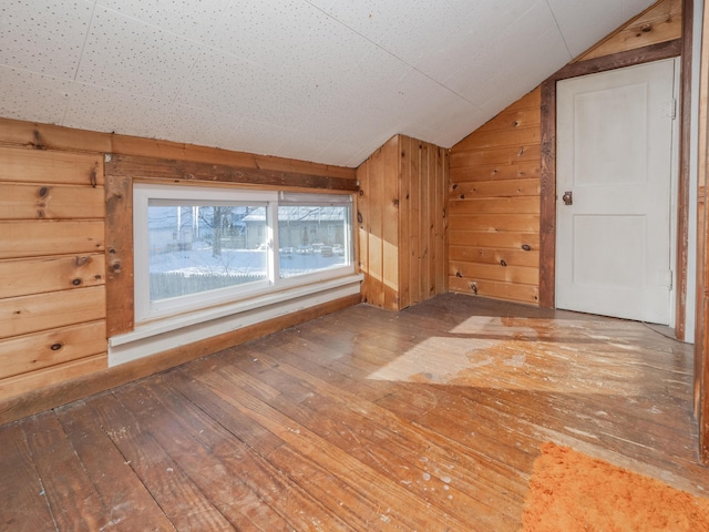 additional living space with wood walls, lofted ceiling, and wood-type flooring