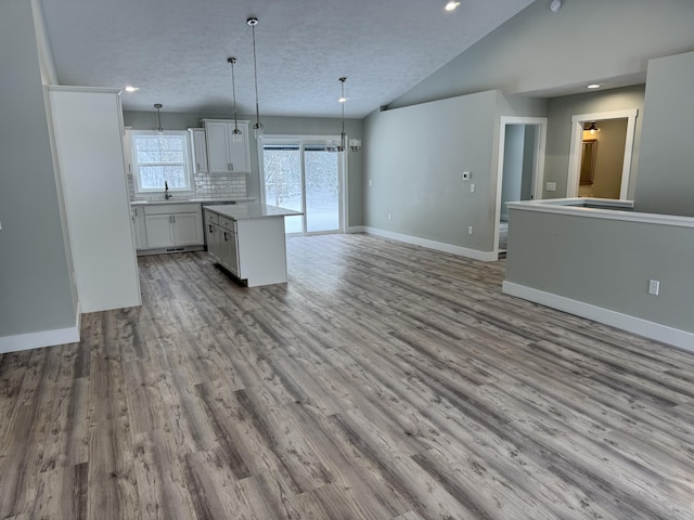 kitchen featuring lofted ceiling, backsplash, a kitchen island, hanging light fixtures, and white cabinets