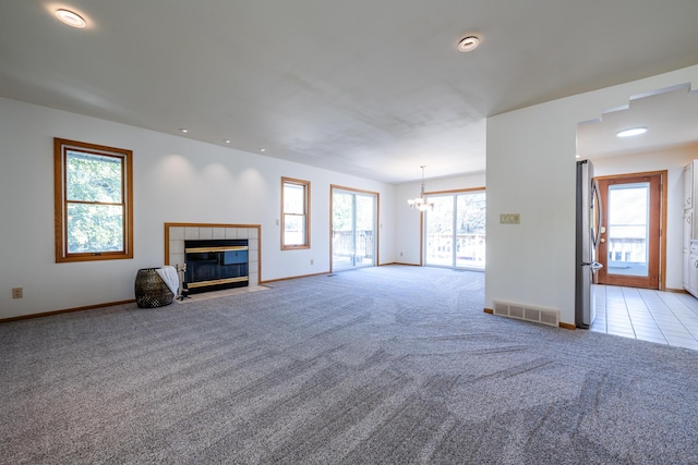 unfurnished living room featuring light carpet, a notable chandelier, and a tile fireplace