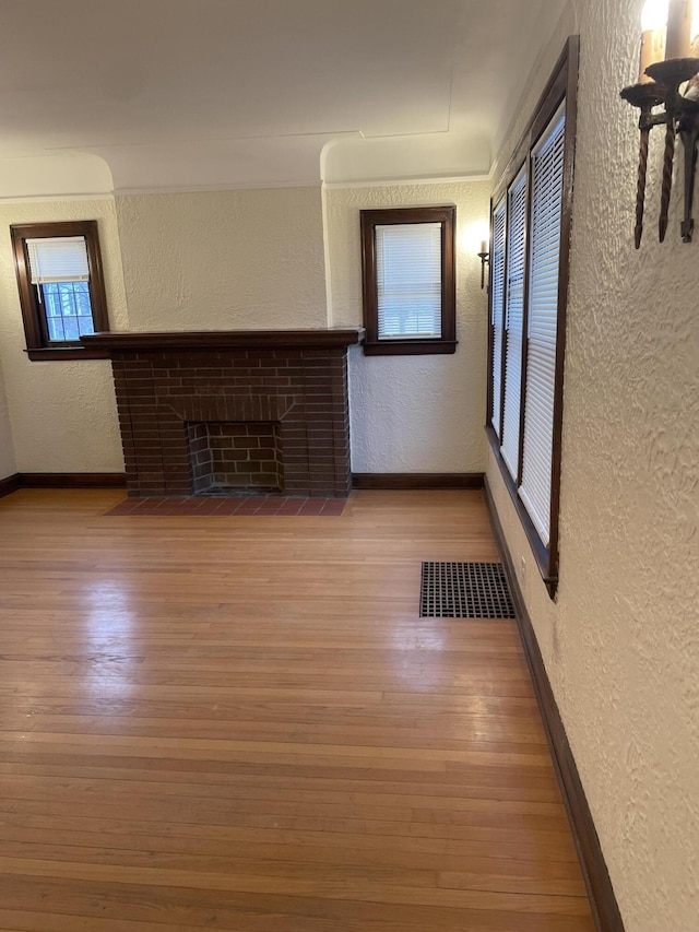 unfurnished living room featuring a brick fireplace, a wealth of natural light, and hardwood / wood-style floors