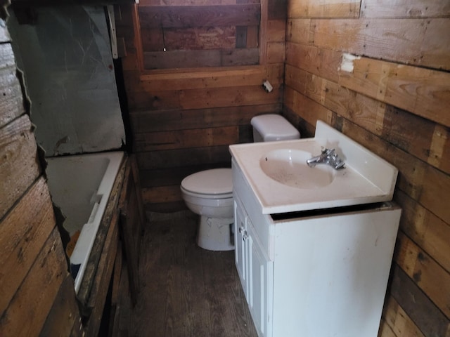 bathroom with toilet, wood walls, a tub to relax in, wood-type flooring, and vanity