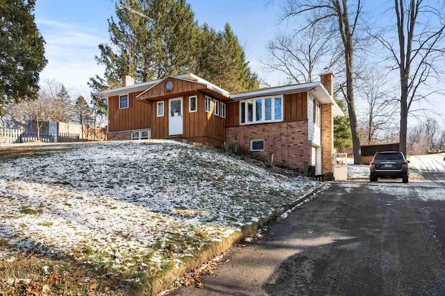 view of front facade featuring driveway, brick siding, a chimney, and board and batten siding