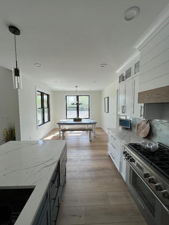 kitchen featuring white cabinetry, light hardwood / wood-style floors, tasteful backsplash, hanging light fixtures, and light stone countertops