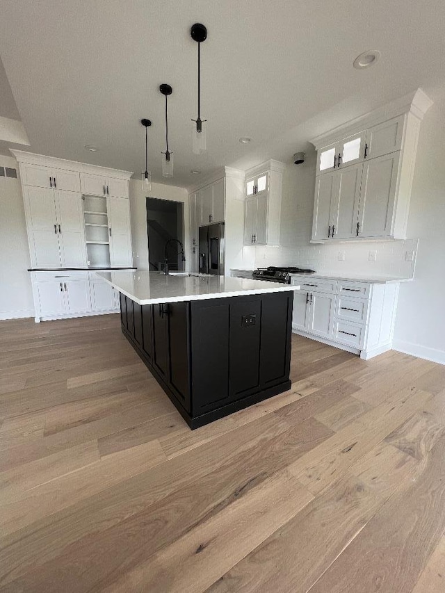 kitchen featuring pendant lighting, white cabinetry, light wood-type flooring, a large island, and stainless steel fridge