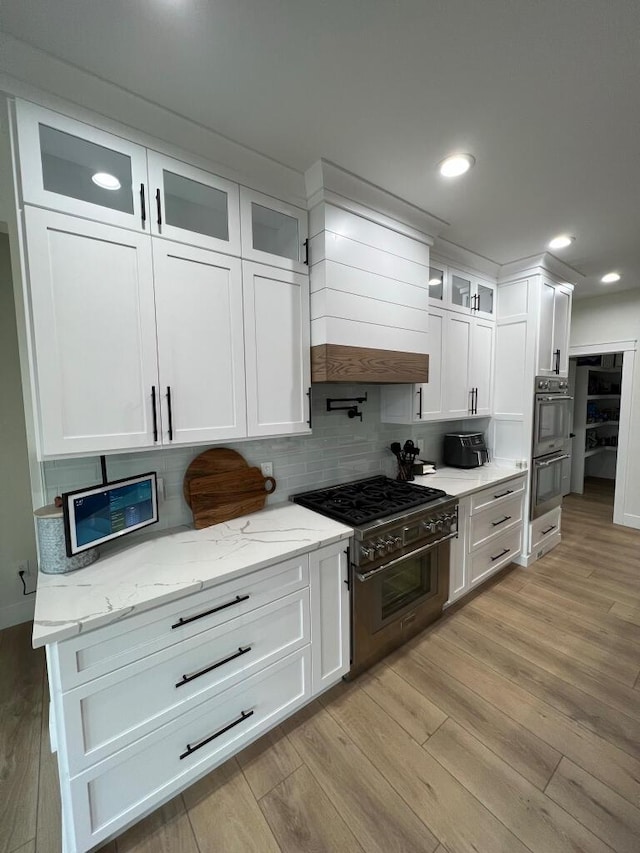 kitchen featuring light stone countertops, white cabinets, stainless steel appliances, light hardwood / wood-style floors, and backsplash